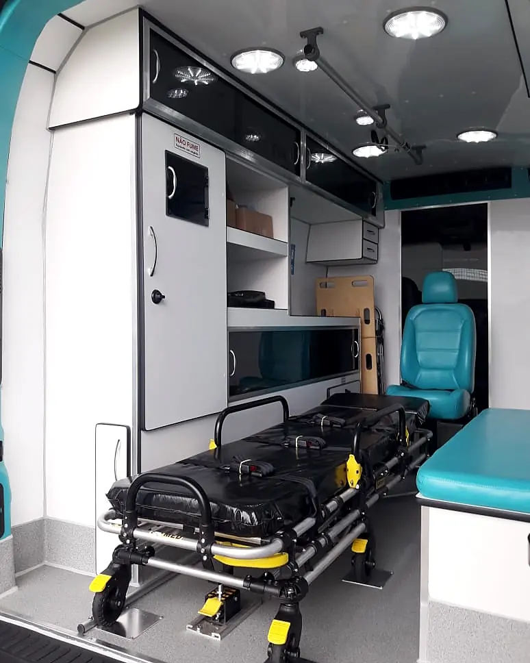 Interior de ambulância com armários, maca, poltrona e iluminação de LED no teto